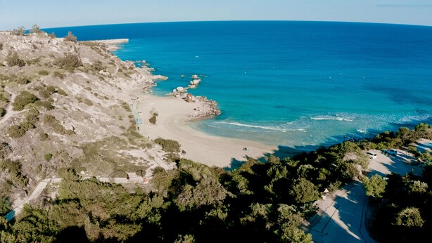 An aerial view of a coastal area with a beach, rocky terrain, and dense greenery. - Kalliopi is a contemporary villa, at Konnos Beach , within Periyiali Resort. (Protaras)