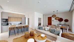 A modern kitchen with a central island, bar stools, and a dining area with a sofa and table. - Kalliopi is a contemporary villa, at Konnos Beach , within Periyiali Resort. (Protaras)