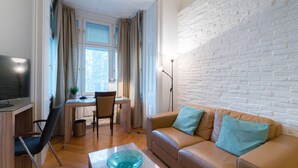 Ein Wohnzimmer mit einer Couch, einem Fernseher, einem Schreibtisch und einer Ziegelwand.