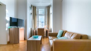 A modern living room with a flat-screen TV, wooden furniture, a sofa, and a view through a window with curtains. - Vienna Residence, City Hall - Parliament #6410 (Vienna)