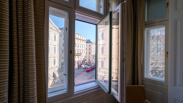 A room with large windows, a view of a street with buildings, and a chair. - Vienna Residence, City Hall - Parliament #6410 (Vienna)