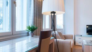 Un salon moderne avec une table en verre, un canapé, un lampadaire et un téléviseur posé sur un meuble.