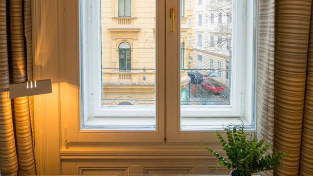 Une pièce dotée d’une grande fenêtre, d’une plante en pot posée sur le rebord de la fenêtre et offrant une vue sur les bâtiments environnants.