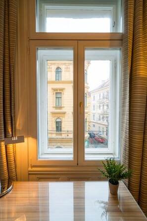 Ein Zimmer mit großem Fenster, einem Blumentopf auf der Fensterbank und Blick auf Gebäude.