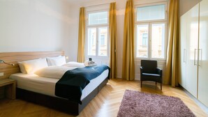 A hotel room with a bed, a chair, a wardrobe, and a window with curtains. - Vienna Residence, City Hall - Parliament #6414 (Vienna)