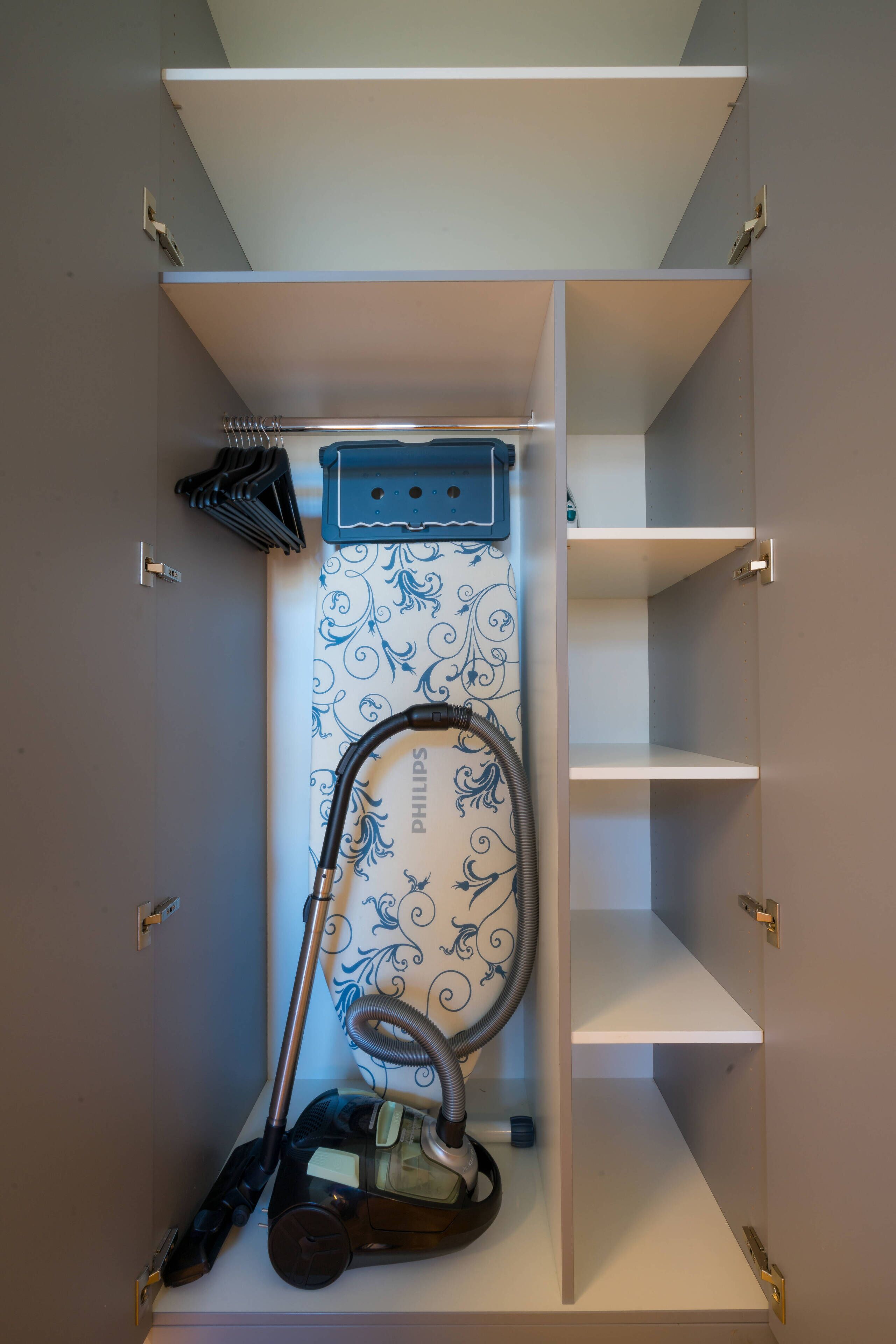 A closet with a vacuum cleaner, a blue dustpan, and a Philips-branded appliance.
