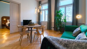 Een moderne woonkamer met een eethoek, grote ramen, een groene bank en een potplant.