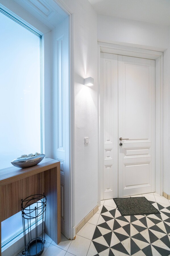 A hallway with a geometric patterned floor, a white door, and a wall-mounted light fixture.