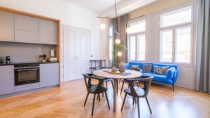 Et moderne køkken med indbygget ovn, et spiseområde med et rundt bord og stole, samt en blå sofa med udsigt til det fri.