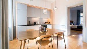 A modern kitchen with wooden cabinets, a dining table with chairs, and pendant lights.