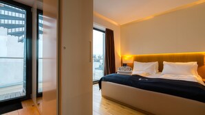 Een moderne hotelkamer met een groot bed, een nachtkastje en uitzicht op de stad door een groot raam.