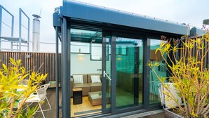 Een moderne buitenruimte met een glazen omheining, een houten terras en een zithoek met een bank en stoelen.