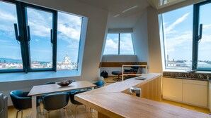 A modern room with a long wooden desk, two chairs, a small table with a bowl, and a view of a cityscape through large windows. - Vienna Residence, City Hall - Parliament #6420 (Vienna)