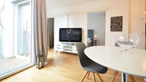 A modern living room with a flat-screen TV, a dining table with chairs, and a large window with curtains. - Vienna Residence, Donaust.- United Nations #6251 (Vienna)