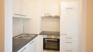 A compact kitchen with white cabinets, a stainless steel sink, a built-in oven, and a modern pendant light. - Vienna Residence, Donaust.- United Nations #6251 (Vienna)