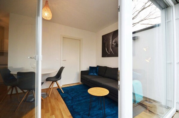A modern living room with a sofa, a small round table, and a glass door leading to a balcony.