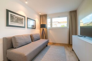 A modern living room with a grey sofa, a floor lamp, a TV on a white cabinet, and framed pictures on the wall. - Vienna Residence, Hietzing - Schönbrunn #6361 (Vienna)