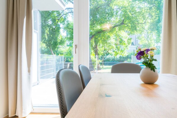 A dining area with a table and chairs, a vase with flowers, and a view of trees and a fence. - Vienna Residence, Hietzing - Schönbrunn #6361 (Vienna)