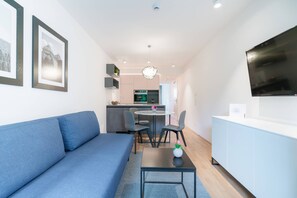 Sala de estar moderna com um sofá azul, uma mesinha com um vaso e uma área de cozinha ao fundo.