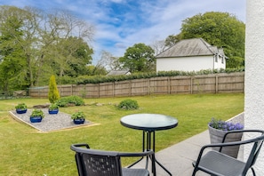 Un jardin avec un petit espace patio, une clôture en bois et une maison blanche.