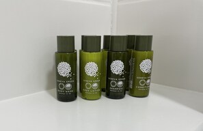 Quatre bouteilles de gel douche, de lotion et de shampoing de la marque Geneva Green, disposées sur une étagère blanche.