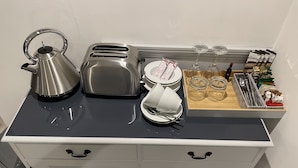 A kitchenette with a kettle, toaster, and tea set on a black countertop. There are wine glasses and a tray of snacks on the right. - Stunning, Contemporary 1 Bedroom En-suite Annexe (Plymouth)