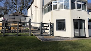 A modern two-story house with a large glass balcony, a wooden fence, and a well-maintained lawn. - Stunning, Contemporary 1 Bedroom En-suite Annexe (Plymouth)