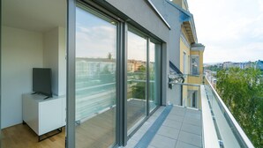 A modern apartment with large sliding glass doors, a flat-screen TV on a white cabinet, and a city view. - Vienna Residence, Hietzing - Schönbrunn #6375 (Vienna)