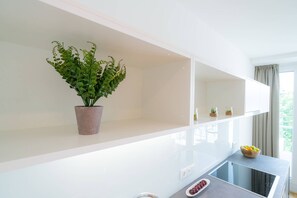 Une cuisine moderne avec des meubles blancs, une plante en pot et un panier de fruits posé sur le plan de travail.