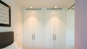 Un dormitori amb un llit, un armari blanc de dues portes i un capçal.