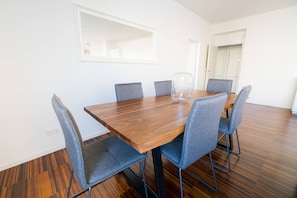 Een eetruimte met een houten tafel en zes grijze fauteuils.