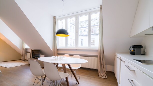 A modern kitchen with white cabinetry, a round dining table with chairs, and a large window with curtains. - Vienna Residence, City Park - Belvedere #2535 (Vienna)