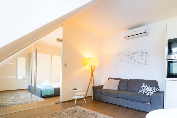 A modern living room with a grey sofa, a standing lamp, and a wall-mounted air conditioner. - Vienna Residence, City Park - Belvedere #2534 (Vienna)