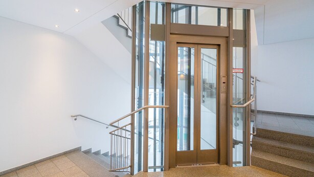 A modern elevator with glass panels, a metal handrail, and a sign indicating elevator access. - Vienna Residence, City Park - Belvedere #2534 (Vienna)