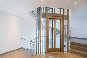 A modern elevator with glass panels, a metal handrail, and a sign indicating elevator access. - Vienna Residence, City Park - Belvedere #2534 (Vienna)