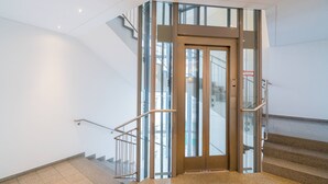 A modern elevator with glass panels and metal handrails, leading to a staircase.