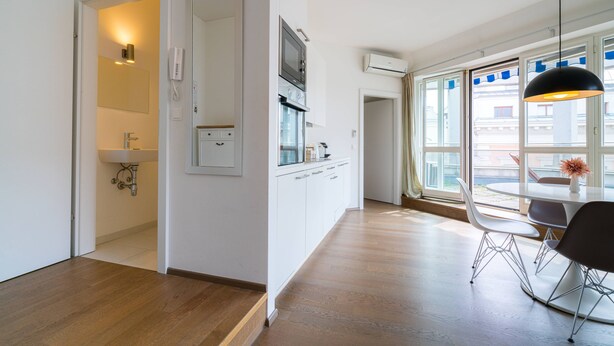 A modern kitchen with white cabinets, a built-in oven, and a large window with a view of buildings.