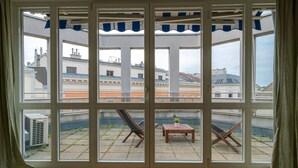 A room with a large window overlooking a courtyard with a table, chairs, and a potted plant.