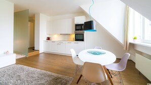 A modern kitchen with white cabinets, a microwave, and an oven. There is a dining area with a white table and chairs, and a ceiling light fixture. - Vienna Residence, City Park - Belvedere #2441 (Vienna)