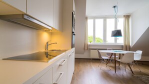 A modern kitchen with white cabinets, a stainless steel sink, and a built-in oven. There is a dining area with a white table and chairs, and a window with curtains. - Vienna Residence, City Park - Belvedere #2441 (Vienna)