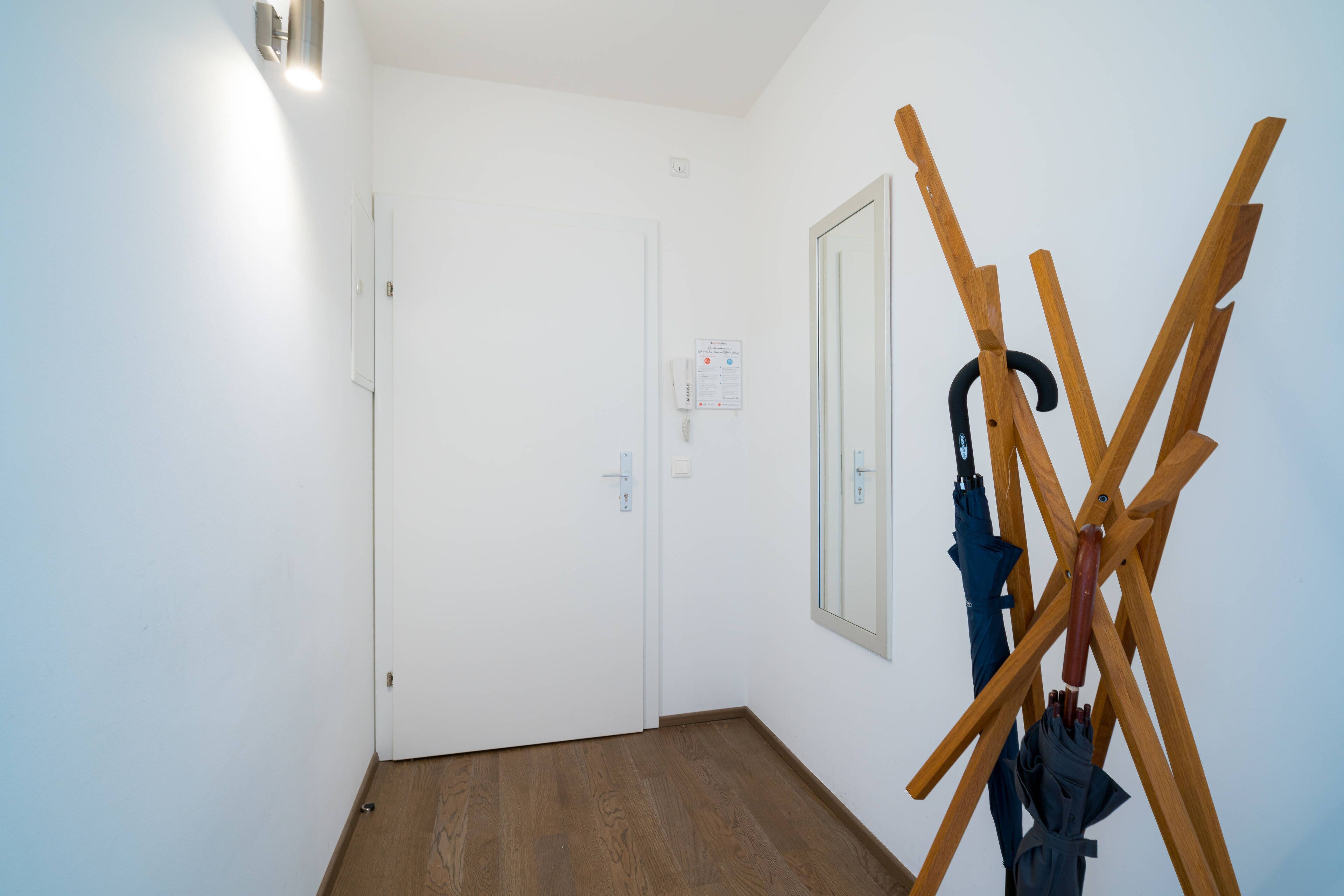 A hallway with a wooden floor, white walls, and a door with a notice.