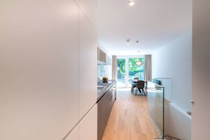 A modern kitchen with a glass partition, wooden flooring, and a dining area with a table and chairs.