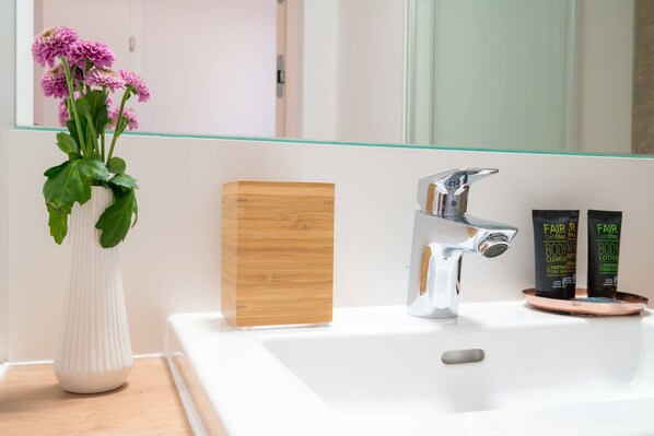 A bathroom with a white sink, a modern faucet, a wooden block, and two bottles of body lotion.