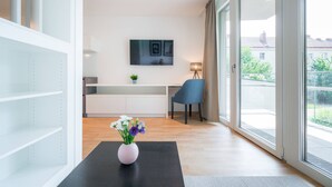 Ein modernes Wohnzimmer mit einem schwarzen Tisch, einer Blumenvase, einem Fernseher an der Wand und einem Balkon mit Aussicht.