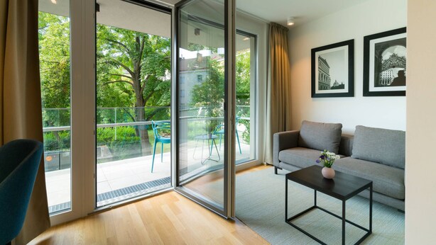 Ein modernes Wohnzimmer mit einem grauen Sofa, einem schwarzen Couchtisch und einer Glastür, die auf einen Balkon mit Sitzmöbeln führt.