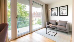 Ein modernes Wohnzimmer mit einer Couch, einem Couchtisch und einem Sessel. An der Wand hängen zwei gerahmte Bilder, und eine Schiebeglastür führt auf einen Balkon.