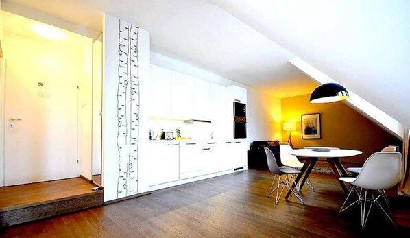 Una cocina moderna con armarios blancos, un comedor con una mesa redonda y dos sillas, y un techo con tragaluces.