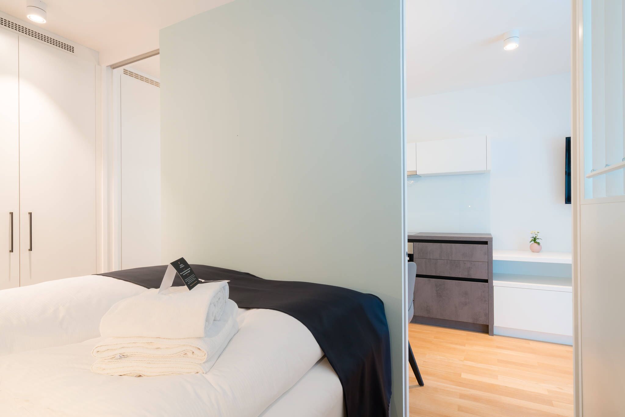 A modern hotel room with a bed, a desk, and a kitchenette.