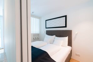Une chambre d’hôtel avec un lit, une tête de lit, une fenêtre avec des stores et un tableau encadré au mur.