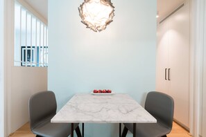 Un espace repas moderne avec une table en marbre, deux chaises grises, un luminaire décoratif et une assiette de pommes rouges.